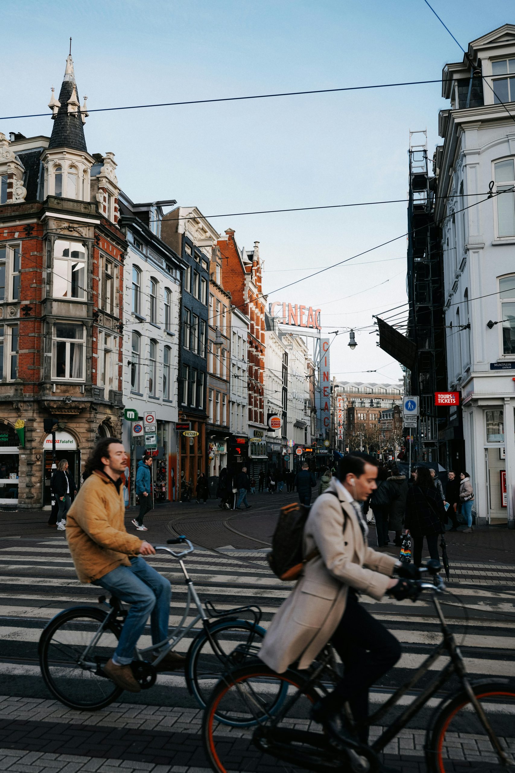 People cycling on a busy street in Amsterdam with iconic architecture in the backdrop.